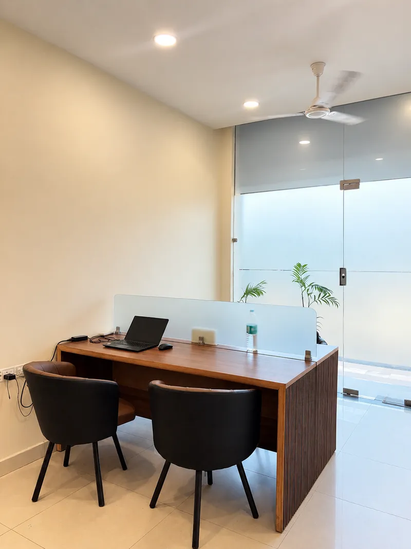 Coworking desk with a laptop near the frosted glass entrance and indoor palms